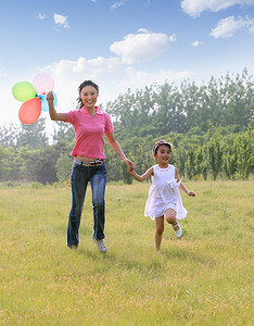 东方女人和孩子手拿气球在草地上跑