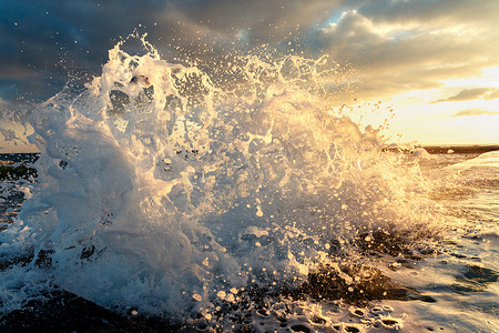 海浪撞到了一个旧的防波堤特写镜头，在夕阳的背景上