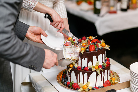 甜饼摄影照片_木桌上有浆果的婚礼蛋糕。新娘和新郎在餐厅的宴会上切甜饼。一块