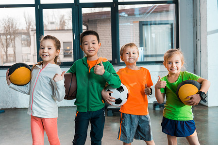 快乐的多文化儿童在体育馆里举球的正面景象