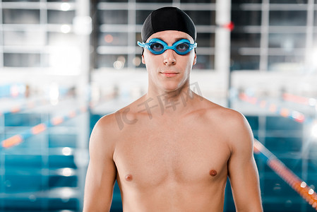 穿着护目镜，戴着泳帽，看着镜头的英俊游泳选手 