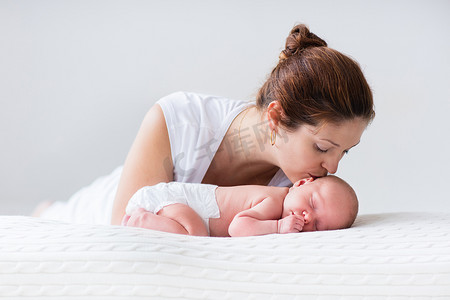 刚出生的男孩摄影照片_年轻的母亲和刚出生的婴儿，在白色的卧室里