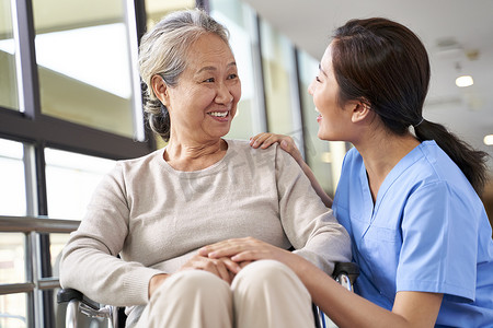 nursing摄影照片_friendly caregiver of nursing home talking to asian senior woman in hallway