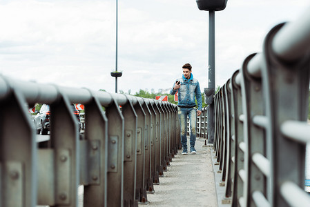 英俊潇洒的男人在走桥道时使用智能手机的选择性聚焦