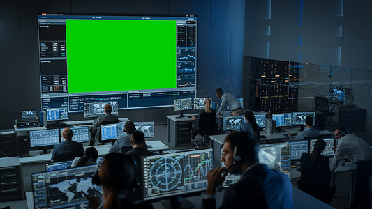 大型绿色屏幕水平造型在飞行控制中心的房间里，有飞行主任和其他在计算机上工作的控制器。在充满展示的监控室工作的工程师小组.