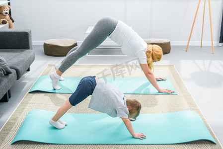 母亲和小男孩练习向下面对狗在瑜伽垫上的位置