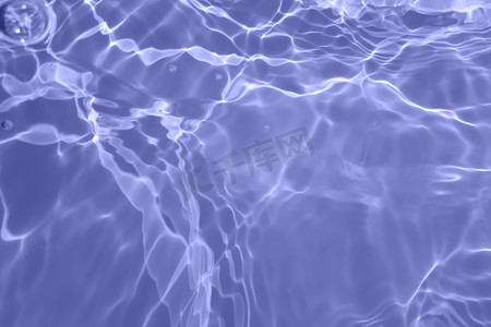 水彩水面摄影照片_Defocus模糊了透明的蓝色清晰平静的水面纹理与水花和气泡。潮流抽象的自然背景.阳光下的水波有复制空间.蓝色水彩斑斓
