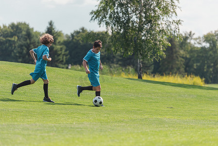 穿蓝色运动服的朋友在绿草地上踢足球 