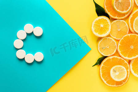 蓝色和黄色背景的白色药丸和柑橘类水果概览，从健康食品中提取维生素的概念