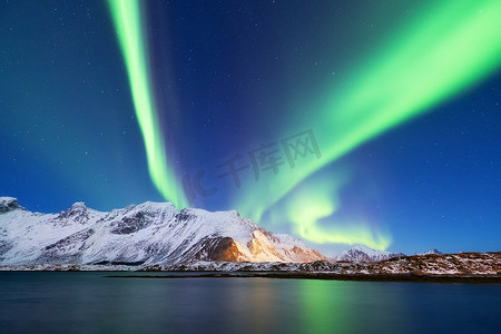 的灯光摄影照片_罗弗敦群岛上的北极极光, 挪威。山上的绿色北极光。夜空中的极地灯光。夜间冬季景观与极光和倒影在水面上。自然背景在挪威