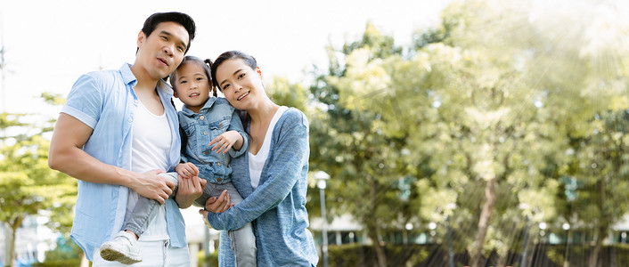在暑假期间，亚洲家庭的父亲、母亲和女儿在公园里开心地笑着。每个人都穿着蓝色衬衫。拥抱对方表现出爱心，关心家人的健康.