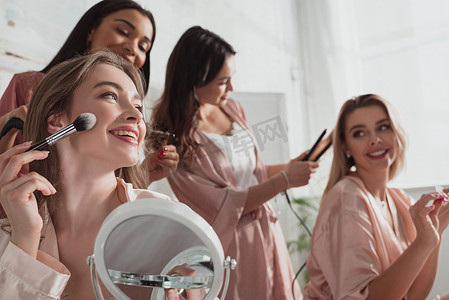 在单身派对上，多民族女性在房间里用化妆品刷化妆、做发型的选择性焦点