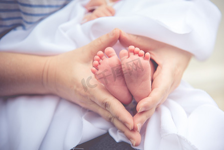 母亲双手抱着新生儿小而柔软的皮肤婴儿脚。爱和感情的概念。产妇与健康主题.
