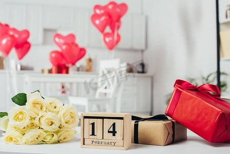 与丝带, 玫瑰花束和日历的礼品盒与2月14日日期在桌子上与心形气球在背景