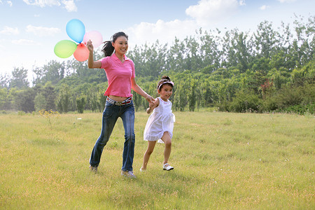 东方女人和孩子手拿气球在草地上跑