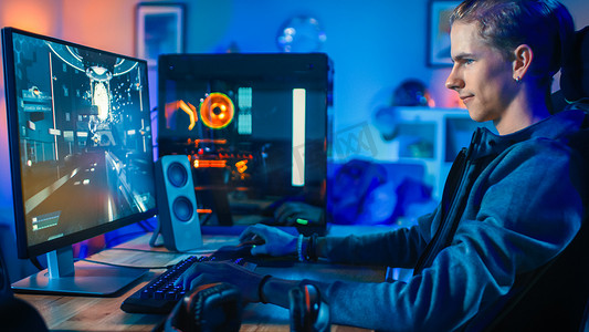 快乐的玩家玩第一人称射击在线视频游戏在他的强大的个人计算机。客房和电脑有五颜六色的霓虹灯灯。在家舒适的夜晚.