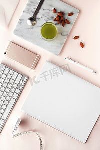 创意杂志摄影照片_创意平坦的工作空间, 风格最小。现代办公桌与计算机, 智能手机, 杂志, 笔记本, 铅笔, tapeline, 杏仁和一杯绿茶在柔和的粉红色背景, 顶部视图