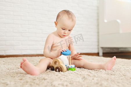 可爱的婴儿穿着一次性尿布坐在地毯上，在白砖墙上玩玩具.