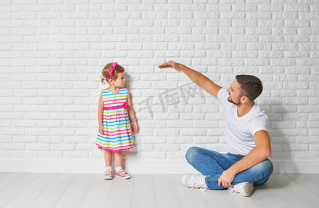 概念。爸爸措施生长的女儿的孩子在一堵墙