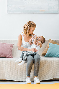 有吸引力的女人坐在沙发上与幼儿男孩喝婴儿奶瓶