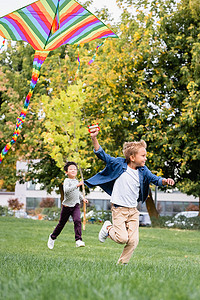 笑男孩牵着放风筝，跑向公园里的亚洲朋友 