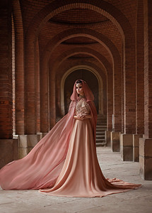 国潮精灵摄影照片_一位身着粉红色长裙、头戴头巾的豪华女士正沿着古老的城堡走廊行走。精灵女王火车的布料在飞舞，在挥手。艺术阴谋和阴谋.