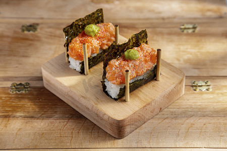 Unwrapped roll with nori, rice, salmon, sauce, tobiko caviar and wasabi on a wooden stand on a wooden table