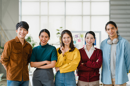 亚洲集团的年轻创意人士，穿着时髦休闲装，双臂交叉地出现在富有创意的办公室工作场所。不同的亚洲男性和女性在创业时站在一起。同事团队精神概念.