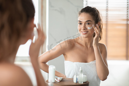 lady摄影照片_Millennial Lady Applying Facial Moisturizer On Cheek Posing In Bathroom