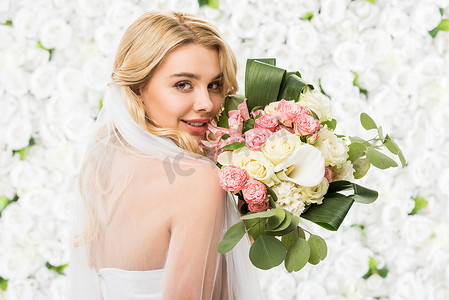 举行婚礼摄影照片_微笑的有吸引力的新娘举行婚礼花束在白色花卉背景