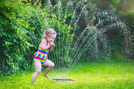 小女孩在玩用花园洒水器
