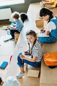 女学生的高视角在学校走廊上学习《论坛报》而她的同班同学坐在后台