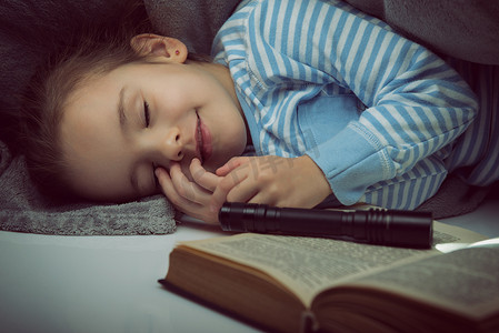 睡觉小女孩摄影照片_小女孩读童话书在夜的盖子之下
