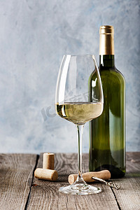玻璃杯中的白葡萄酒，一瓶白葡萄酒和瓶塞，瓶塞上有一个开瓶器，放在一张旧木桌上