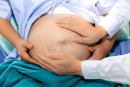 英俊的医生正在检查胎儿的位置通过触摸孕妇腹部在医院。美丽的母亲或怀孕的妇女怀孕九月, 几乎分娩。她呆在医院的房间里