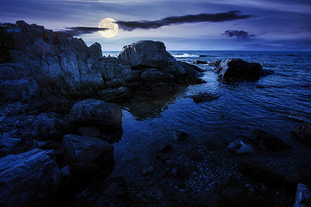 夜晚的海滨风景。巨石在平静的水里。在满月的光下，天上的云彩很少。去一个寂寞的地方放暑假。晴天