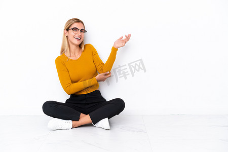 Blonde Uruguayan girl sitting on the floor extending hands to the side for inviting to come
