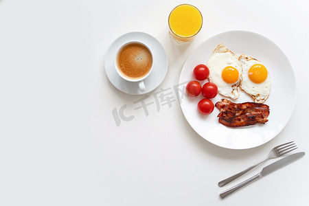 白西红柿摄影照片_美式早餐,两个鸡蛋,咸肉,西红柿,咖啡和橙汁放在白桌上.顶部视图。复制空间.