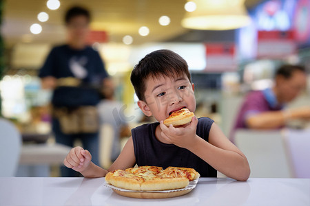 亚洲6-7 岁男孩很高兴吃比萨饼与热奶酪融化在一个木垫在餐厅.