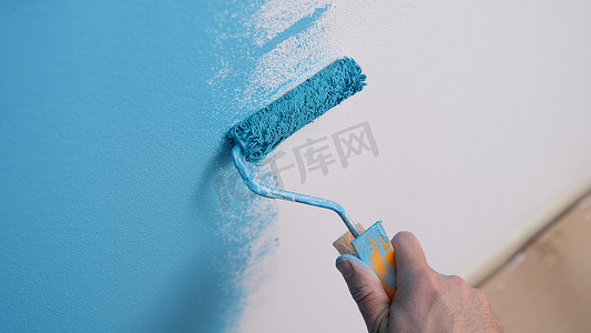 手拿着滚筒,把墙壁涂成蓝色.房屋维修和墙面油漆概念