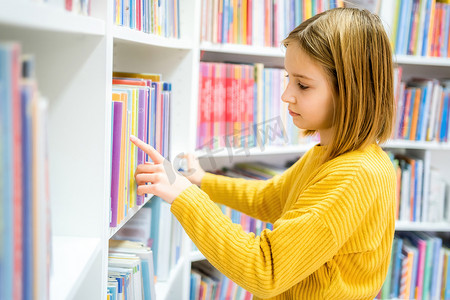 女学生在学校图书馆选书.聪明的女孩选择阅读的文献。书店架子上的书。从书本中学习。学校教育。日常阅读的益处