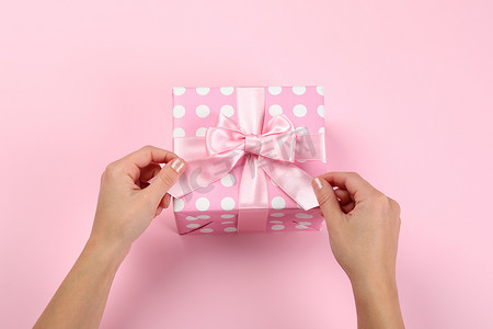 粉红背景的带蝴蝶结的女性手和礼品盒