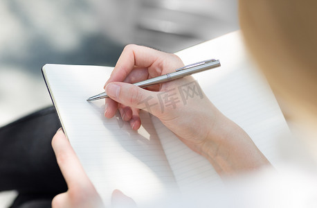 女性坐在室外用笔在空白日记本上用手写单子的服装.