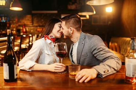 浪漫的夜晚在酒吧, 爱情夫妇在木柜台接吻。情侣们在酒吧里休闲, 丈夫和妻子一起在夜总会放松