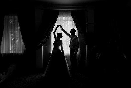 新娘和新郎的剪影在窗口。新娘和新郎跳舞。新婚夫妇。婚礼当天新郎握着新娘的手。这对夫妇跳着华尔兹。婚礼舞蹈彩排