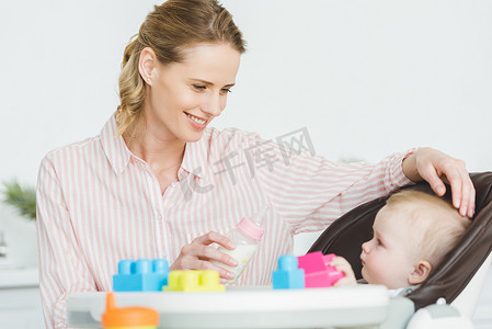 母亲带奶瓶和婴儿的女儿坐在婴儿椅与塑料块