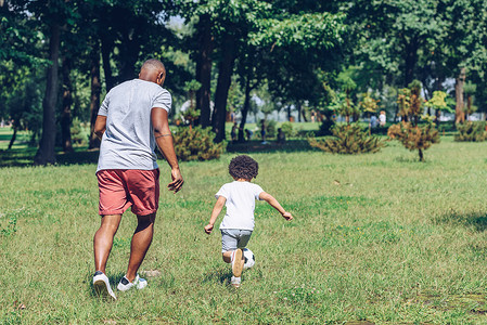 back view of african american father and son playing football in park