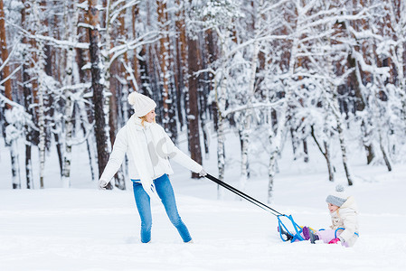 一起看看表情包摄影照片_年轻的母亲和小女孩雪橇在冬天的森林里一起