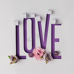 紫罗兰色背景摄影照片_鲜花与字的爱由撕裂的纸在紫罗兰色背景, 情人节概念