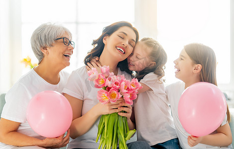 母亲节快乐！孩子们的女儿们在向妈妈和奶奶表示祝贺,祝贺他们送给郁金香花.奶奶，妈妈和女孩们笑着拥抱。家庭假日和团聚.
